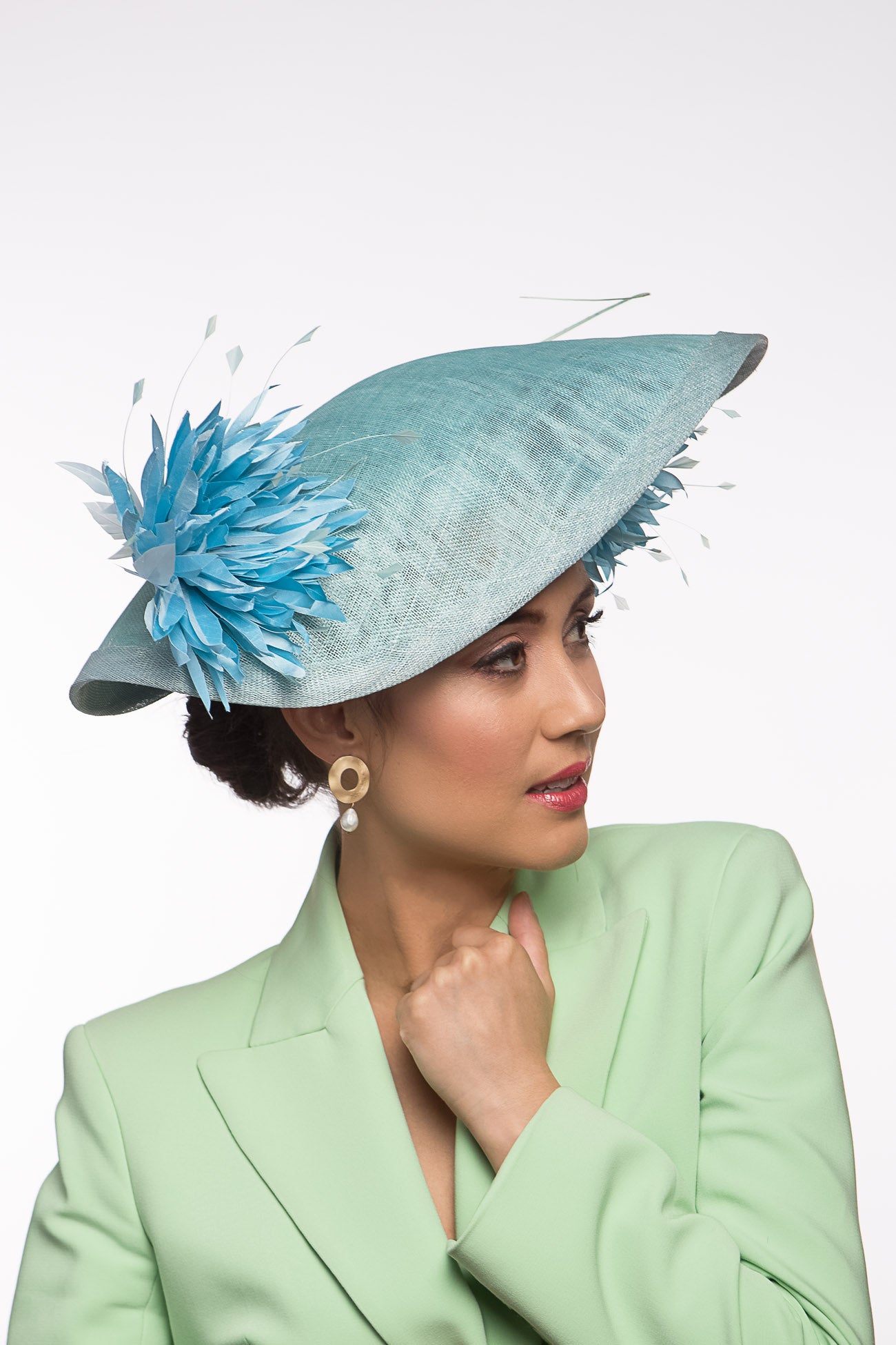 The Pale Blue Asymmetric Picture Hat features a curved oval platter hat and is finished with pom pom chrysanthemums under and on top of the brim.