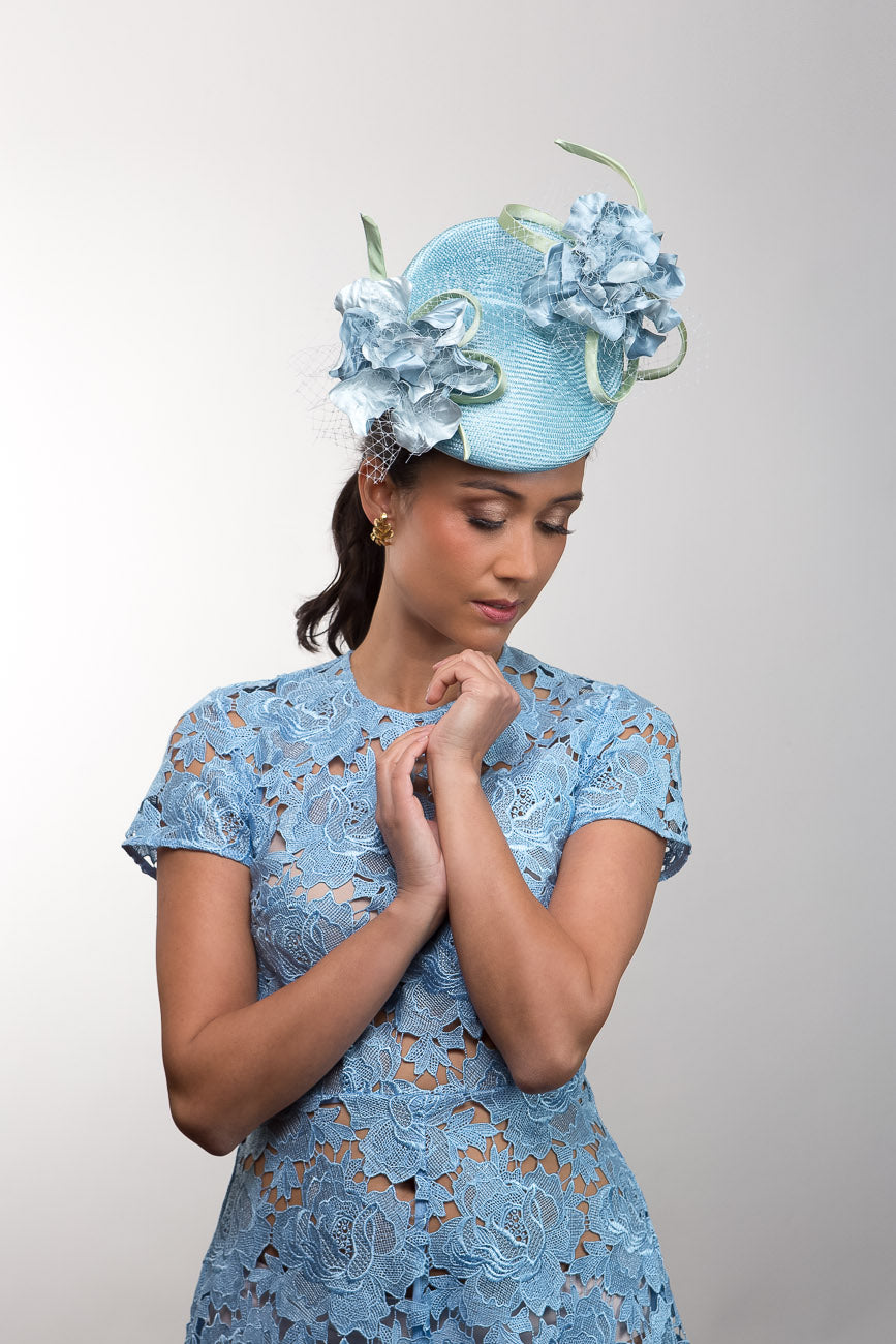 Woman wearing a blue lace dress and matching headpiece with floral details on a plain background