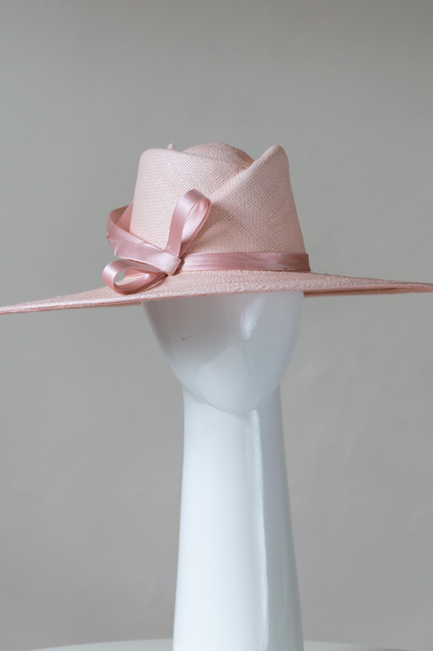The Pink Panama Fedora with Silk Bow is a modern fedora with a sweeping angular crown and a wide flat brim in pastel pink straw