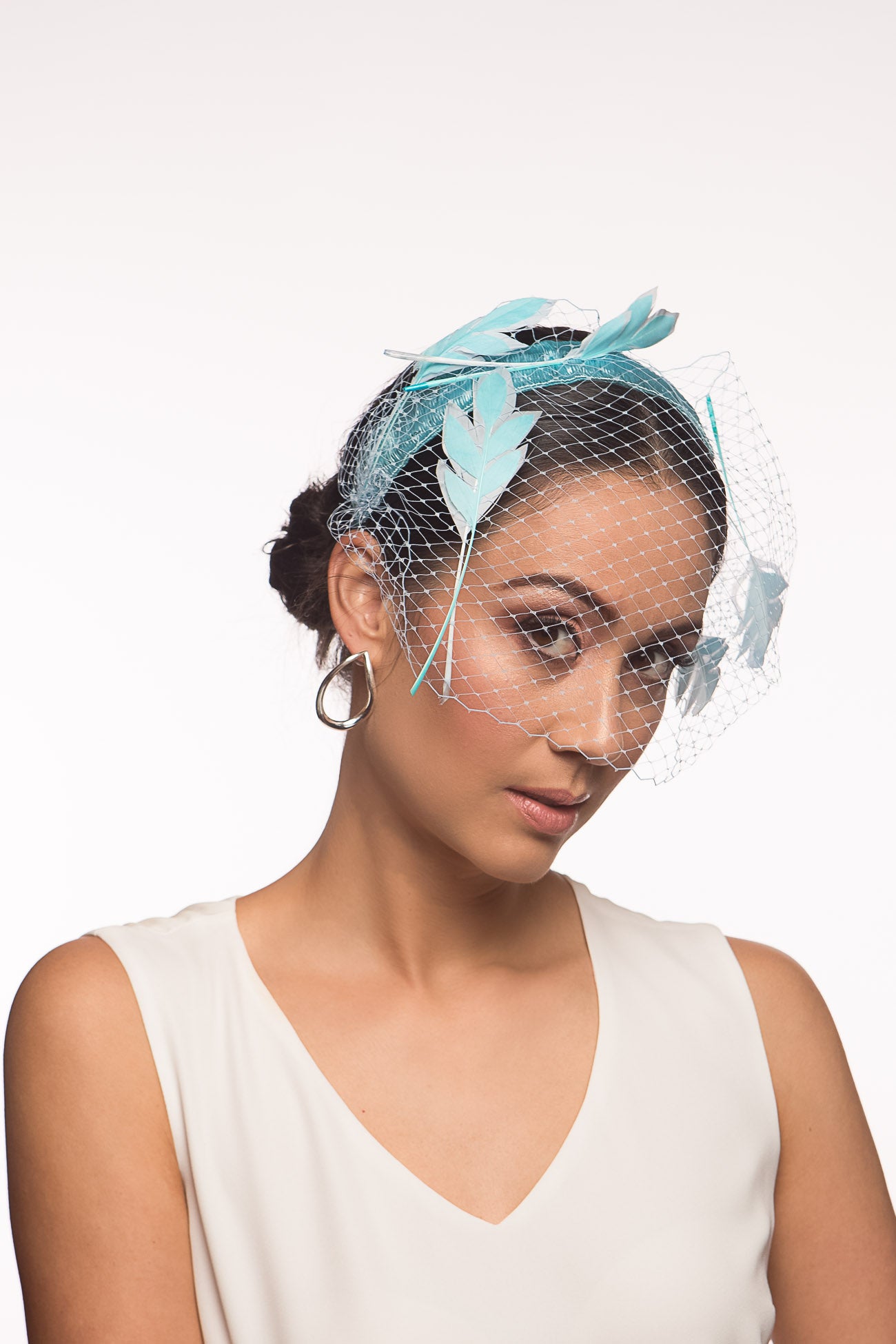 The Veiled Feather Leaf Headband in Blues features a birdcage veil adorned with feather leaves. The sky blue feather leaves are arranged over the pale blue ones