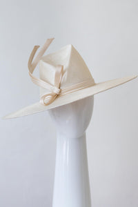 The Cream Fedora with Sweeping Bow is a modern fedora with a high angular concave crown and a sweeping wide brim