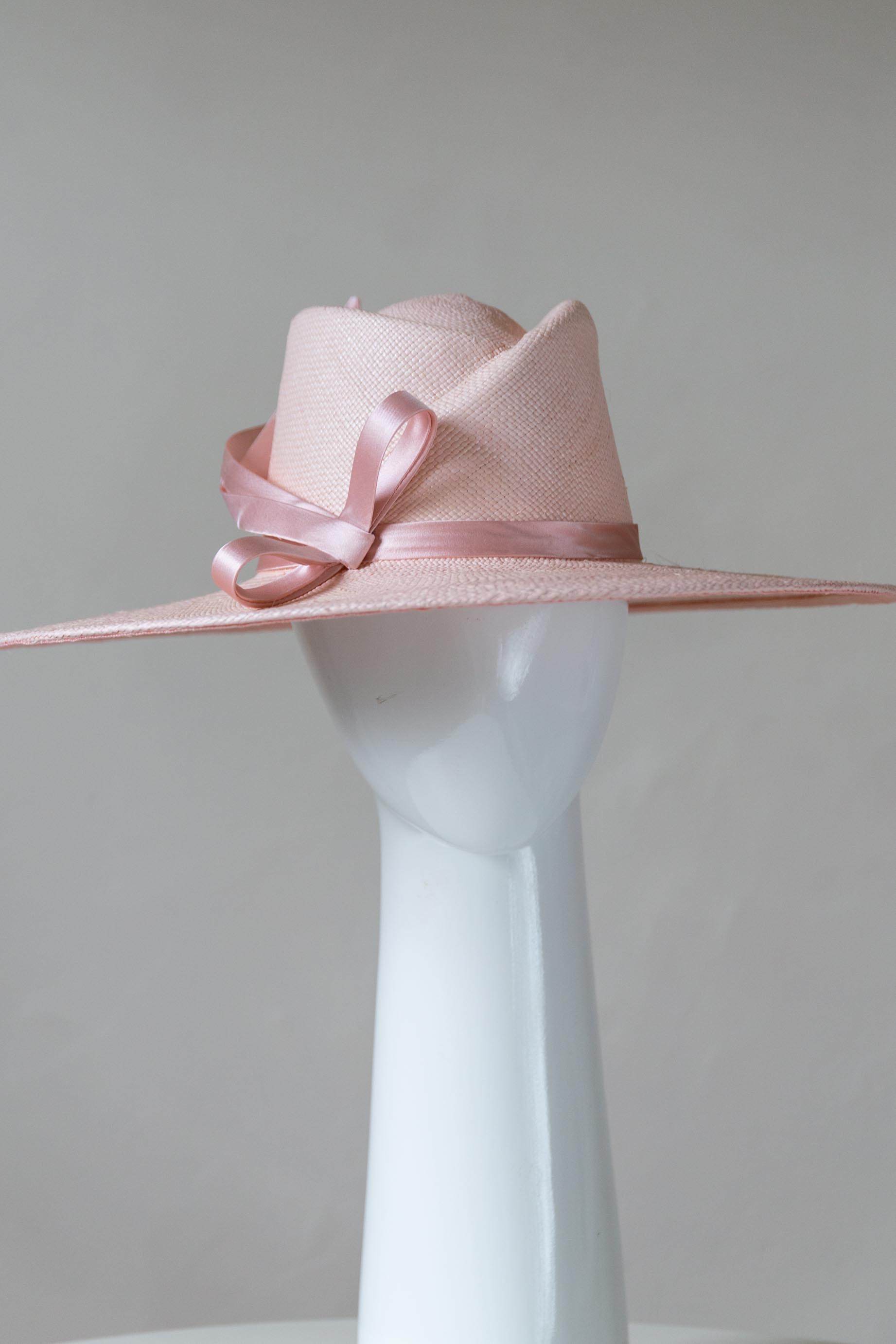 The Pink Panama Fedora with Silk Bow is a modern fedora with a sweeping angular crown and a wide flat brim in pastel pink straw