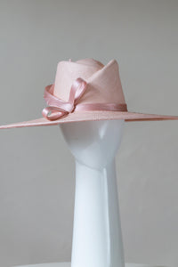 The Pink Panama Fedora with Silk Bow is a modern fedora with a sweeping angular crown and a wide flat brim in pastel pink straw