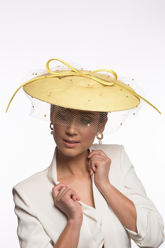 The Yellow Platter Hat with Bow and Veiling features a wide Dior brim with a shallow crown. Trimmed with a lux satin silk bow on across the brim and draped in a fine vintage veiling